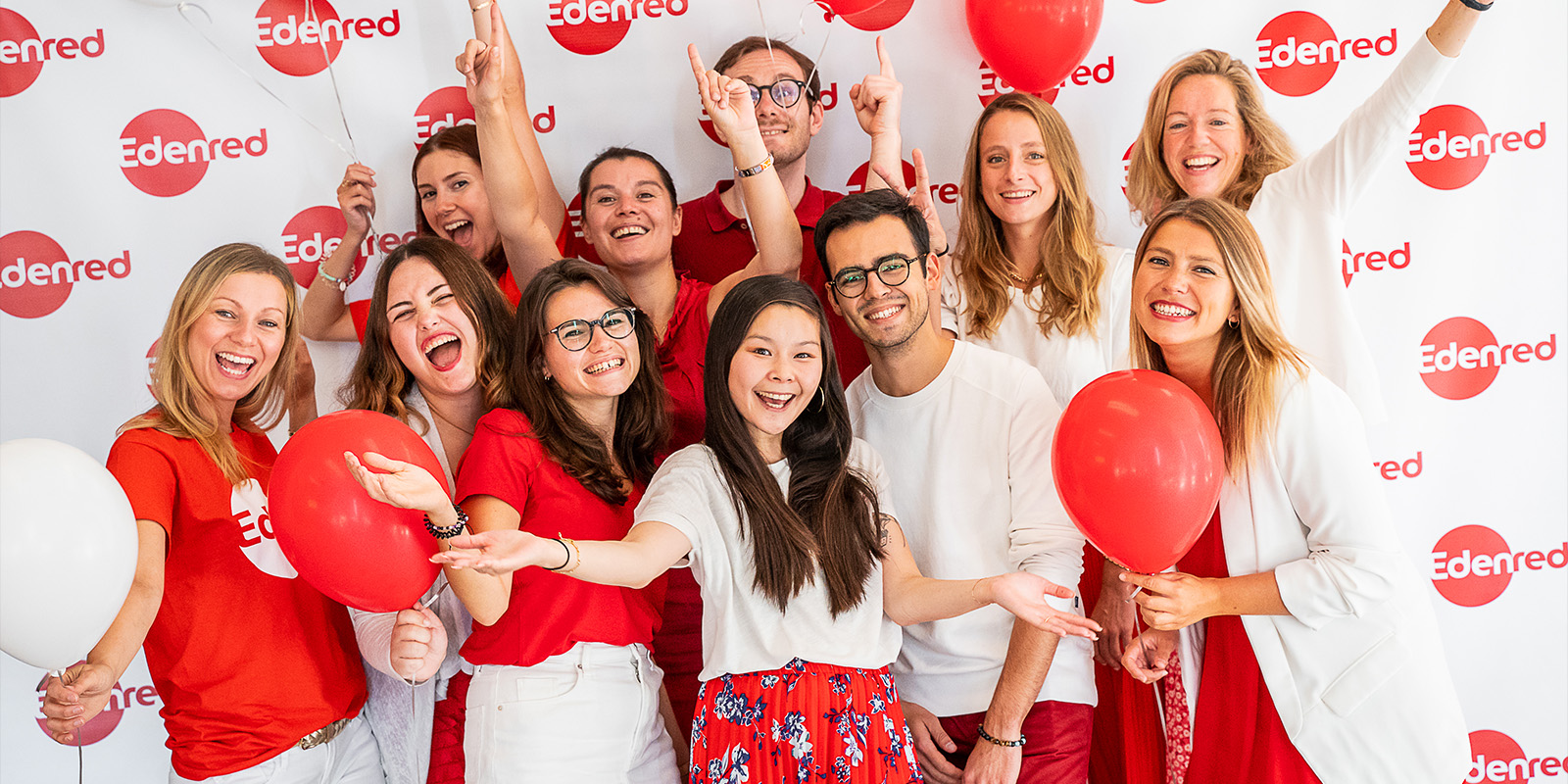 People standing in front of the Edenred fabric holding red balloons