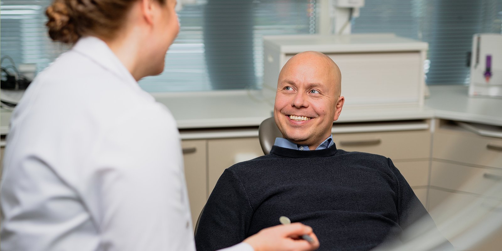 Mies istuu hammashoitotuolissa ja hymyilee leveästi