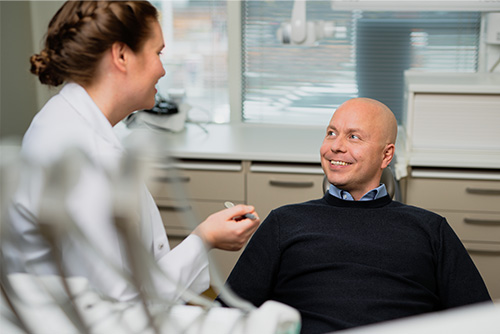 Hammaslääkäri ja hymyilevä mies, joka istuu hammaslääkärin tuolissa