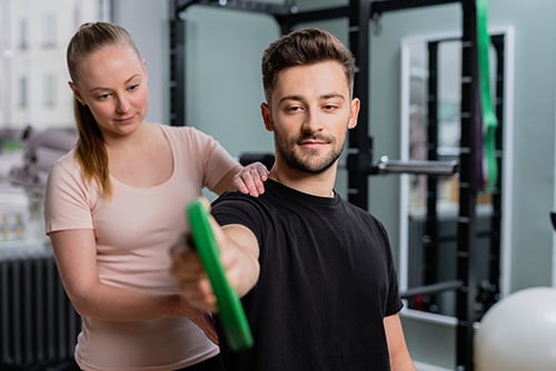 Fysioterapeutti harjoittelee asiakkaan kanssa kuntosalilla