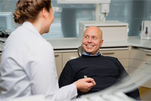 Mies istuu hymyillen hammaslääkärin vieressä